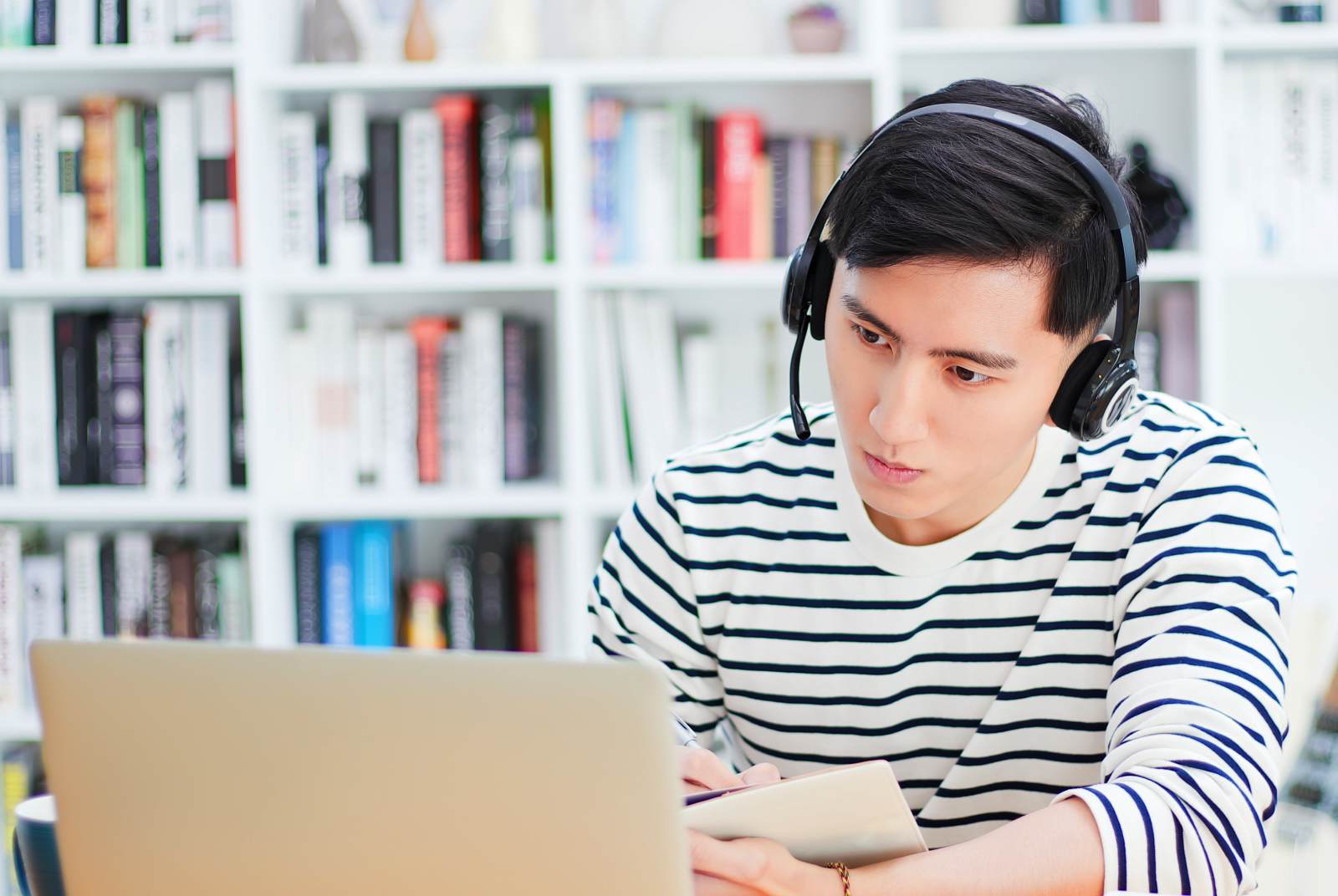 一名戴著耳機的男子正在家庭辦公室的筆記型電腦上工作，訪問一個促進學習和成就的互動式線上課程平台。